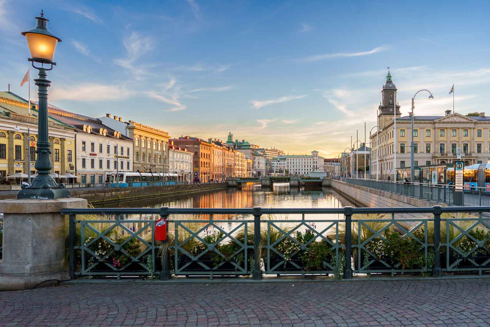 En naturskön vy av en kanal i Göteborg, Sverige, med historiska byggnader och en spårvagn som speglas i vattnet vid solnedgång.