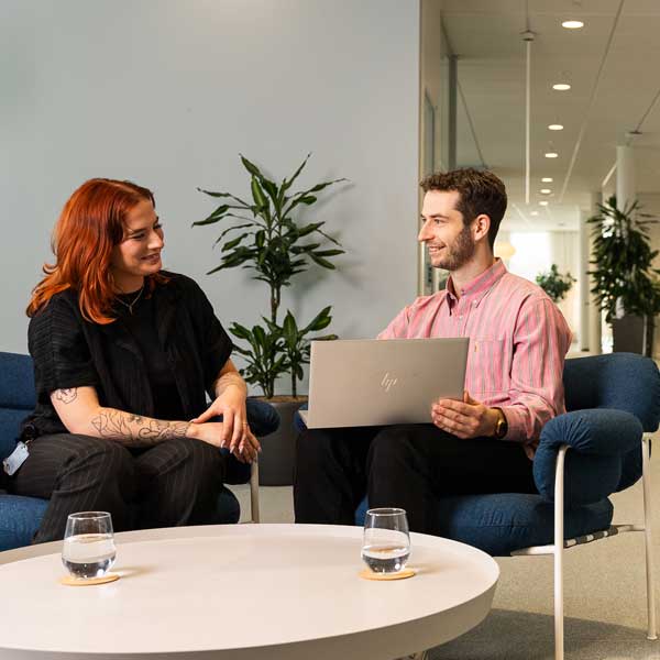 A professional meeting between two individuals. One is working on a laptop while seated next to a coffee table with water glasses.