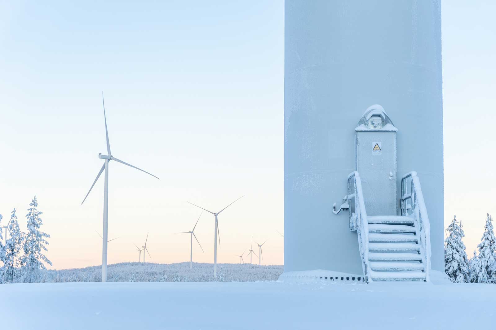 A snowy landscape featuring wind turbines and a wind generator tower with a frosted door and staircase.