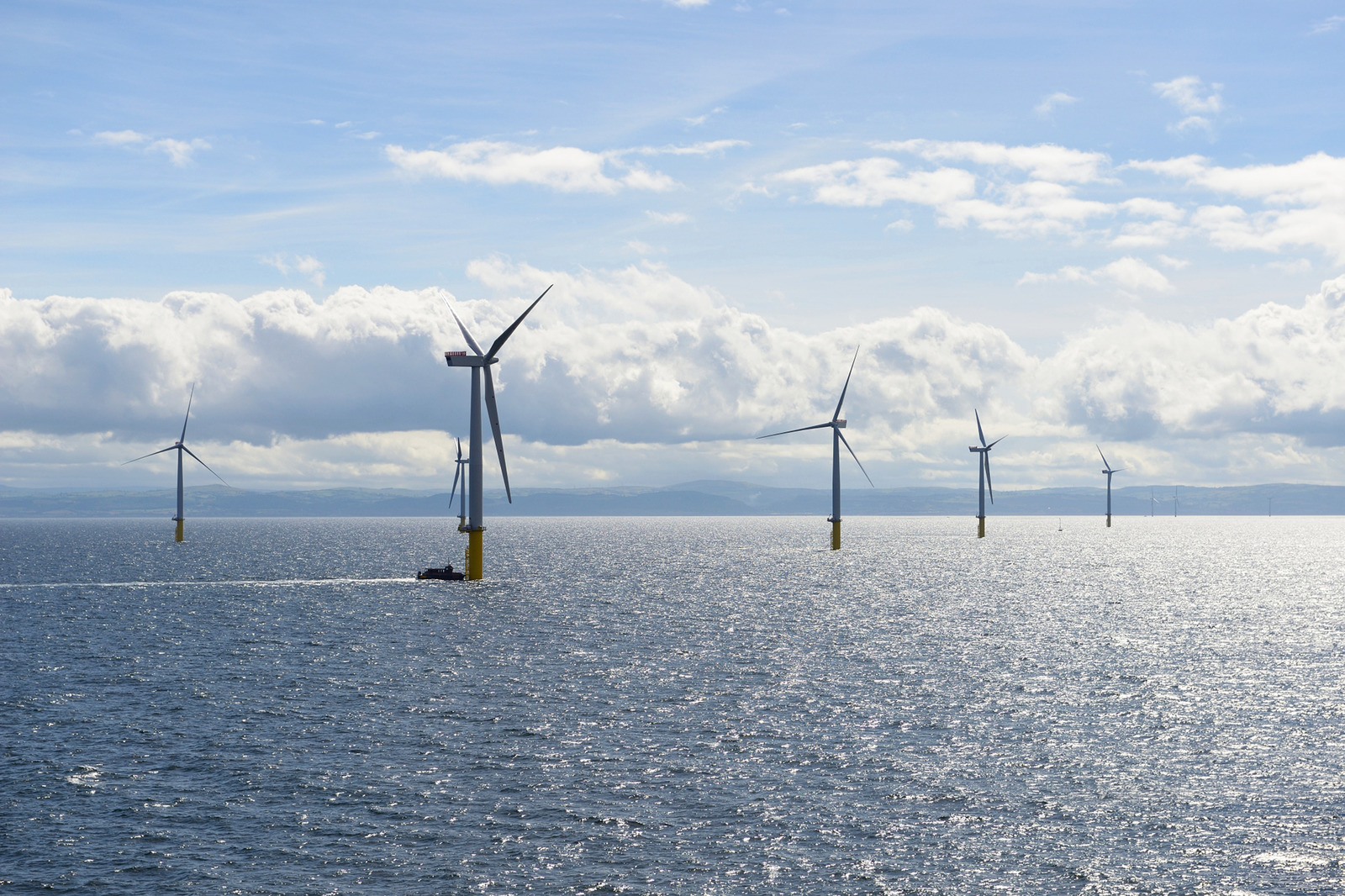 A serene view of offshore wind turbines in the sea under a bright sky with fluffy clouds.