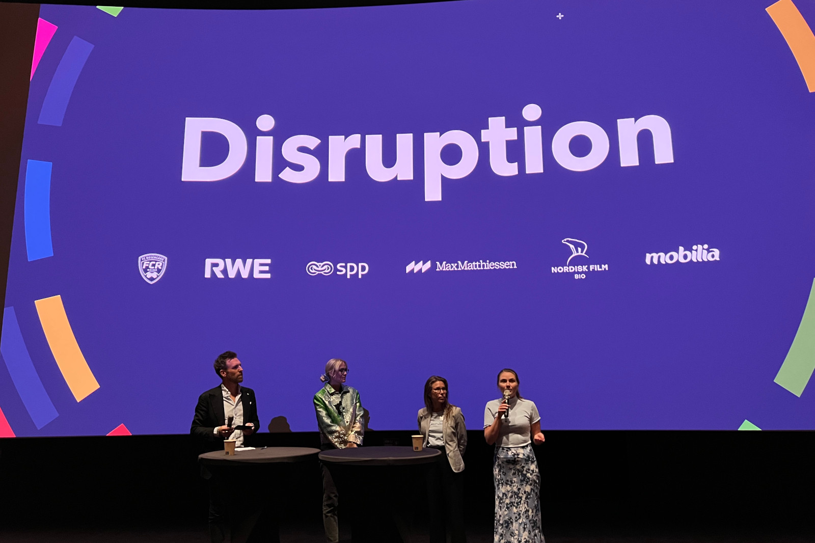 Vid en konferens står fyra talare framför en stor 'Disruption'-banner med företagslogotyper.