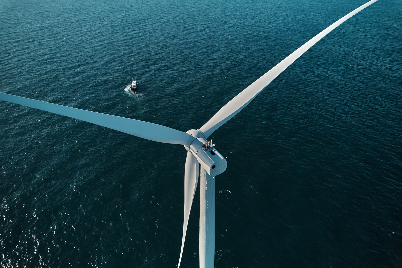 An aerial view of a large offshore wind turbine with a small boat in the ocean, showcasing renewable energy technology.