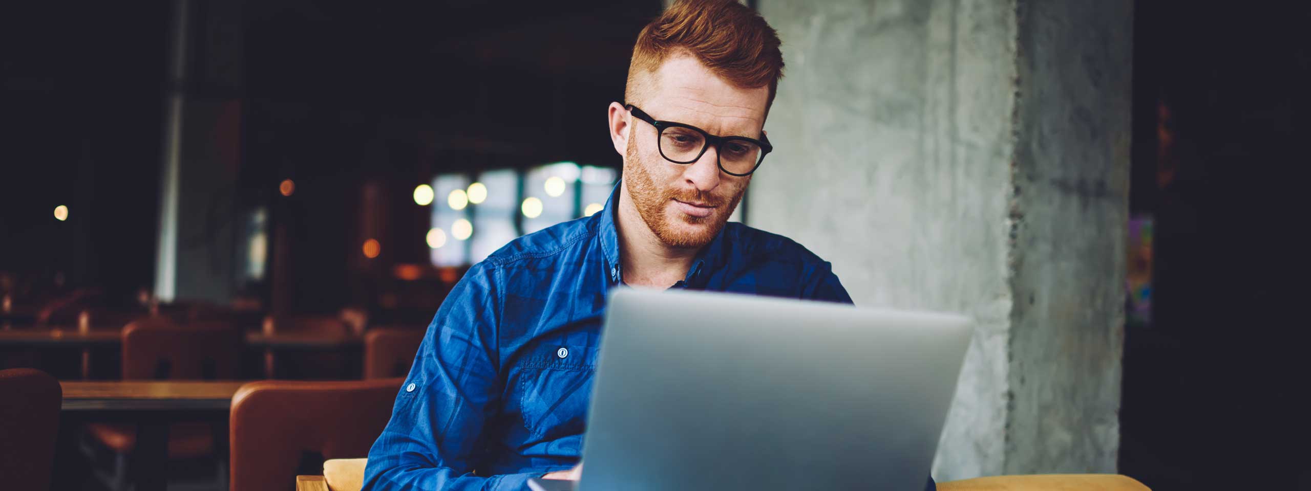 En person sitter vid ett bord och arbetar på en laptop i en mörk miljö med bakgrundsljus.