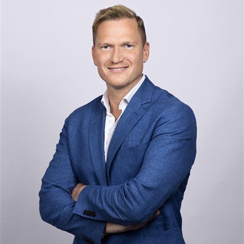 En man i en blå kavaj poserar självsäkert med armarna i kors, vilket visar en professionell framtoning. Porträtt av Klas Lomberg.