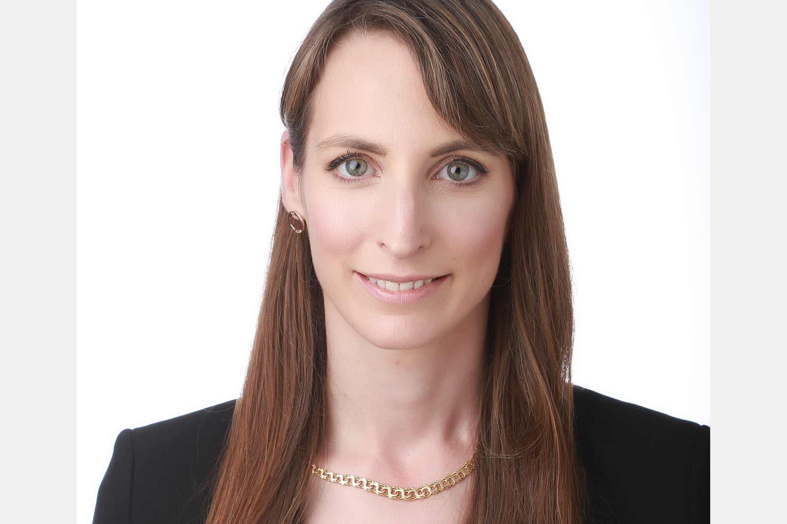 En kvinna med långt brunt hår bär en svart kavaj och ett guldhalsband.