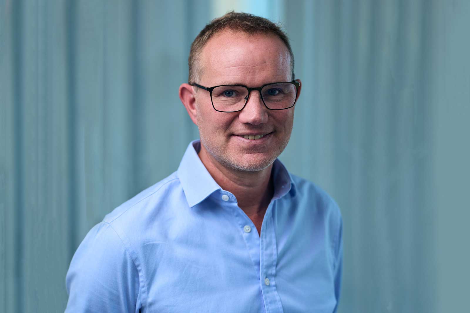 En man i blå skjorta står framför en mjuk blå bakgrund med draperat tyg.